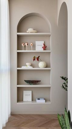 a white shelf filled with vases and other items next to a plant on top of a hard wood floor