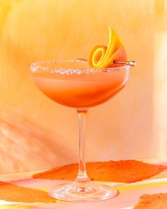 an orange cocktail garnished with sugar in a coupe glass on a yellow and white tablecloth