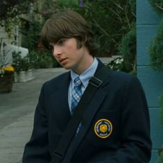 a young man in a suit and tie standing next to a blue wall with trees