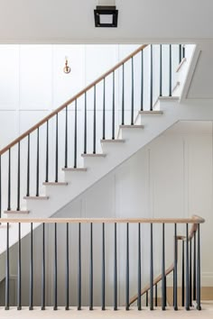 a white staircase with black handrails next to a light on the wall above it