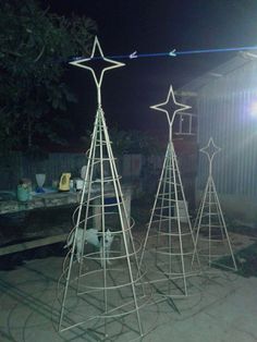 three white metal christmas trees sitting on top of a cement ground