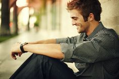 a man sitting on the ground next to a wall with his arms crossed and smiling