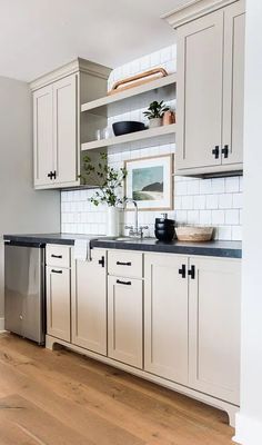 a kitchen with white cabinets and black counter tops, wood flooring and wooden floors