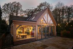 a small wooden house with glass walls and doors on the outside, lit up by string lights