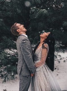 a man and woman standing next to each other in front of snow covered pine trees