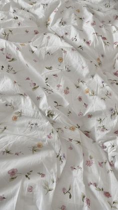 an unmade bed with white sheets and pink flowers