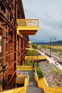 people are walking up and down the stairs in front of an industrial building with yellow railings