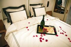 a bed with rose petals on it and a bottle of champagne sitting on the tray