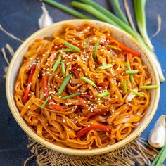 a bowl filled with noodles and vegetables on top of a blue tablecloth next to green onions