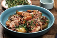 a blue bowl filled with meat and vegetables on top of a wooden table next to two plates