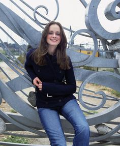 a young woman sitting on top of a metal sculpture in front of a park bench