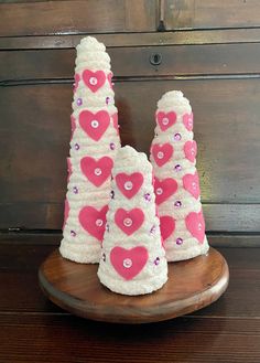 three pink and white knitted cones with hearts on them sitting on a wooden plate