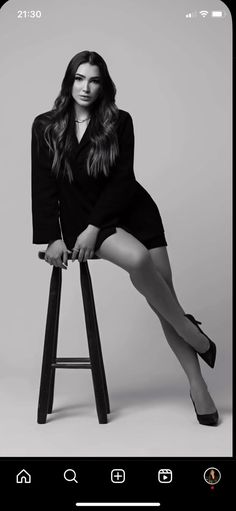 a woman sitting on top of a stool in black dress and high heeled shoes