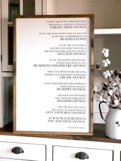 a white vase filled with flowers on top of a table next to a framed sign