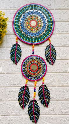 a multicolored dream catcher hanging on the side of a white brick wall next to a potted plant