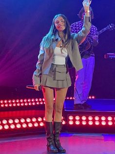 a woman standing on top of a stage with her hand up in the air while holding a microphone