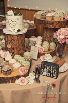 a table topped with lots of cupcakes covered in frosting next to trees