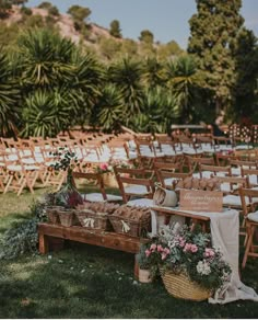 an outdoor ceremony setup with wooden chairs and baskets filled with flowers, greenery and signs