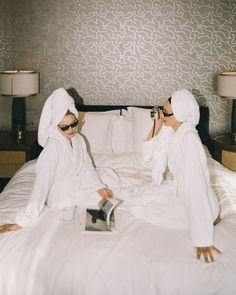 two women in white robes sitting on a bed