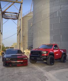 two red and black trucks parked next to each other in front of a silo