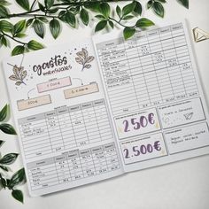 an open planner sitting on top of a table next to some green leaves and plants