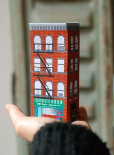 a person holding up a paper model of a building