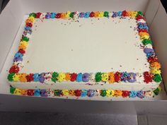 a large sheet cake with white frosting and multicolored icing in a box