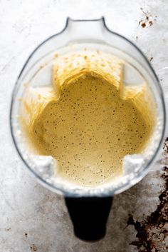 a blender filled with yellow liquid on top of a white countertop covered in dirt