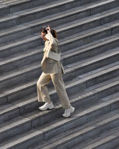 a woman is walking up some steps and talking on her cell phone while wearing a tan suit