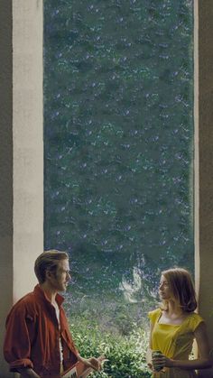 a man and woman standing next to each other in front of a window with water on it