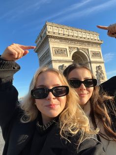 two women standing in front of the eiffel tower with their hands up and pointing