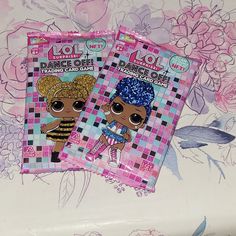 two lol dolls stickers sitting on top of a flowery tablecloth covered surface