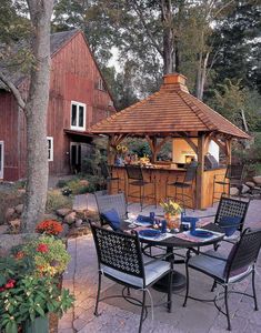 an outdoor dining area with table, chairs and grill in the middle of it next to a red barn