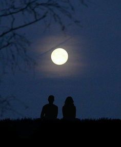 two people sitting on a hill watching the moon