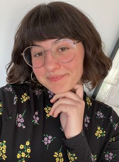 a woman with glasses is posing for the camera while wearing a floral shirt and silver rimmed glasses