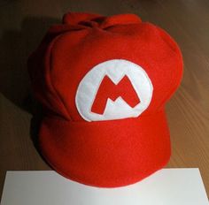 a red mario hat sitting on top of a wooden table next to a white piece of paper