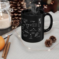 a black coffee mug sitting on top of a table next to pine cones and candles