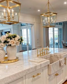 a large kitchen with marble counter tops and gold accents on the cabinets, along with two chandeliers hanging from the ceiling