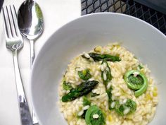 a white bowl filled with rice and green peppers next to silverware on a table