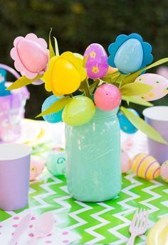 a vase filled with flowers and balloons on top of a green table covered in paper plates