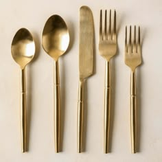 five gold colored forks and spoons on a white surface