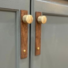 two brass knobs are on the handles of some gray cabinet doors with wood accents