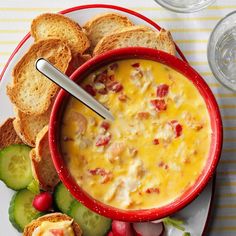 a red bowl filled with soup next to crackers and cucumbers on a plate