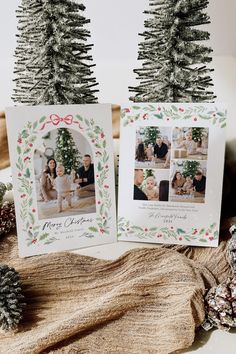 two christmas cards sitting on top of a table next to pine cones and fir trees