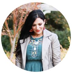 a woman standing in front of a tree wearing a green dress and jacket with beaded necklace