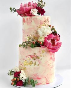 a three tiered cake with pink and white flowers on the top is decorated with greenery