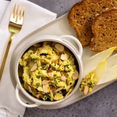 a white plate topped with bread and a bowl filled with food next to a fork