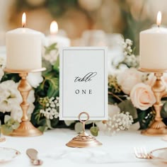 a table topped with candles and flowers next to two small white signs that read table one