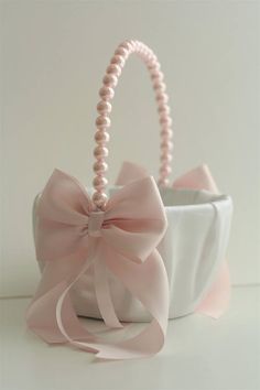 a white basket with a pink bow and pearls on the handle is sitting in front of a white wall