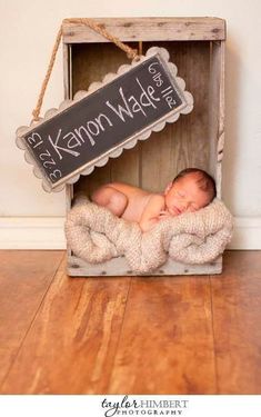 a baby is sleeping in a wooden crate with a chalkboard sign hanging from it's side